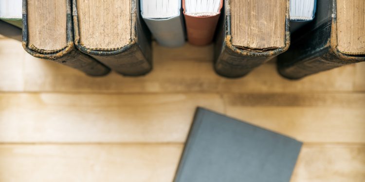 Closed book in front of several books on the table. Top view.